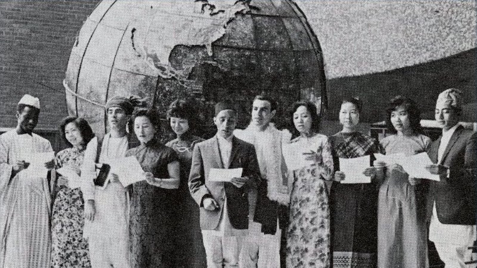 Black and white of a group of international students in their national dress in front of the historic SFS globe.