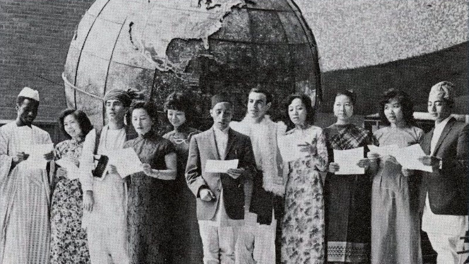 Black and white of a group of international students in their national dress in front of the historic SFS globe.