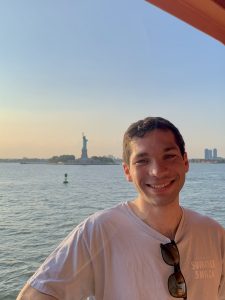 Headshot of Caleb on a boat in front of the Statue of Liberty