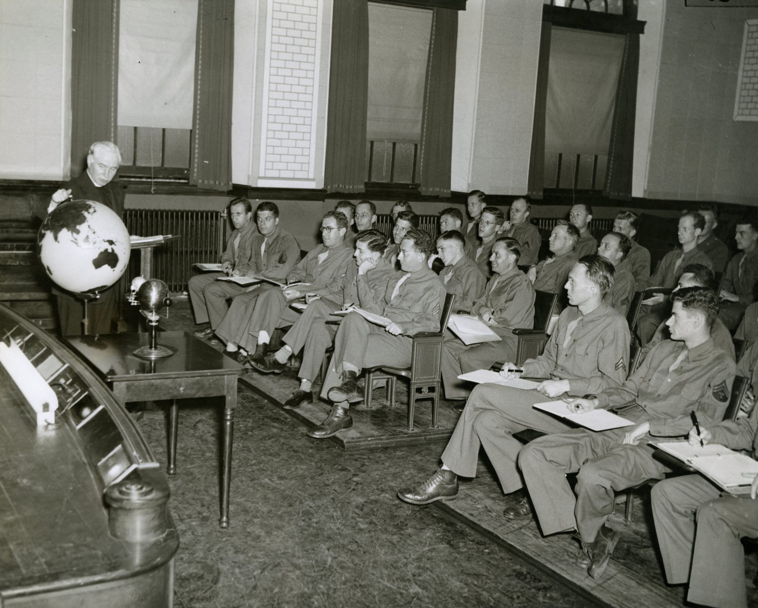 Students in WWII uniform listening to a lecture by Father Walsh in Healy Hall